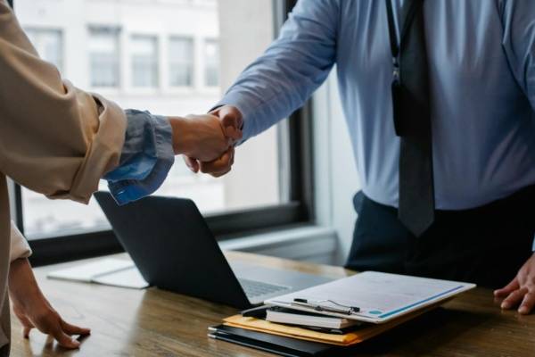 Crop unrecognizable coworkers in formal wear standing at table with laptop and documents while greeting each other before meeting, IT Companies in Nagpur